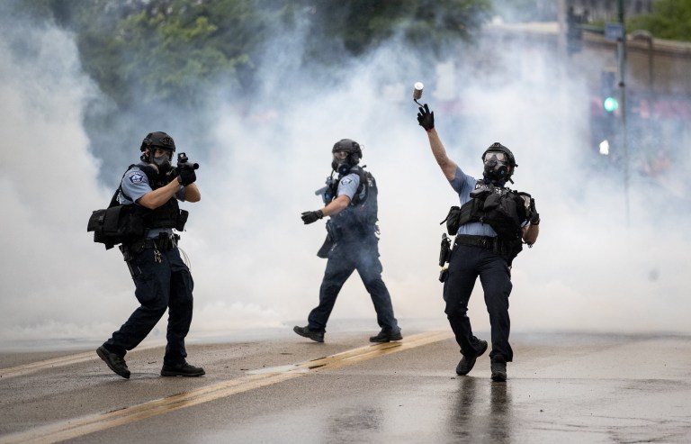 A police officer throws a tear gas canister towards protesters at the Minneapolis 3rd Police Precinct